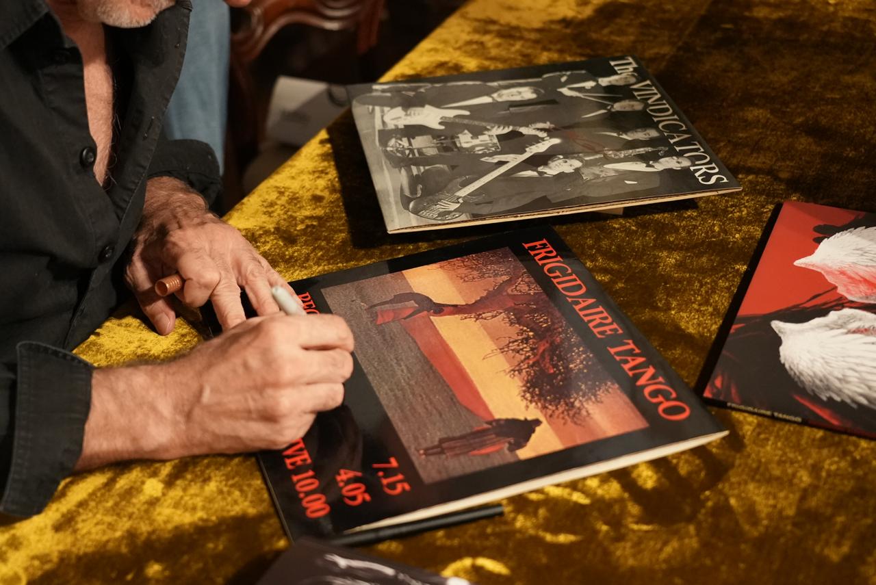 A hand signing a Frigidaire Tango record sleeve, next to a second LP
