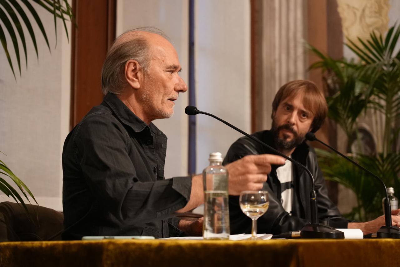 The author pointing across the table while the interviewer listens